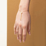 A hand facing down wearing The Slide Heart Bracelet and Delicate Beaded Band in yellow against a tan brown background. 