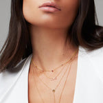 Close-up of a brunette woman's neck wearing a Love Necklace, a Gold Lariat Necklace, and a Custom Gold Necklace - 5 Letters with birthstones, in a white top.