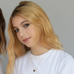 A blonde girl wearing an Enamel Gold Unity Pendant - Small with a white t-shirt against a light grey background. 