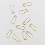 Several Gold Safety Pin Earrings and Pavé Safety Pin Earrings against a light grey background. 