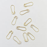 Several Gold Safety Pin Earrings and Pavé Safety Pin Earrings against a light grey background. 