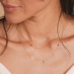 A close-up of a woman’s neck wearing a 14k Gold Asymmetrical Charm Necklace - Star of David with a bead chain, and a Custom Gold Necklace - 5 Letters (L, S, a hand, K and a birthstone), both in yellow gold.